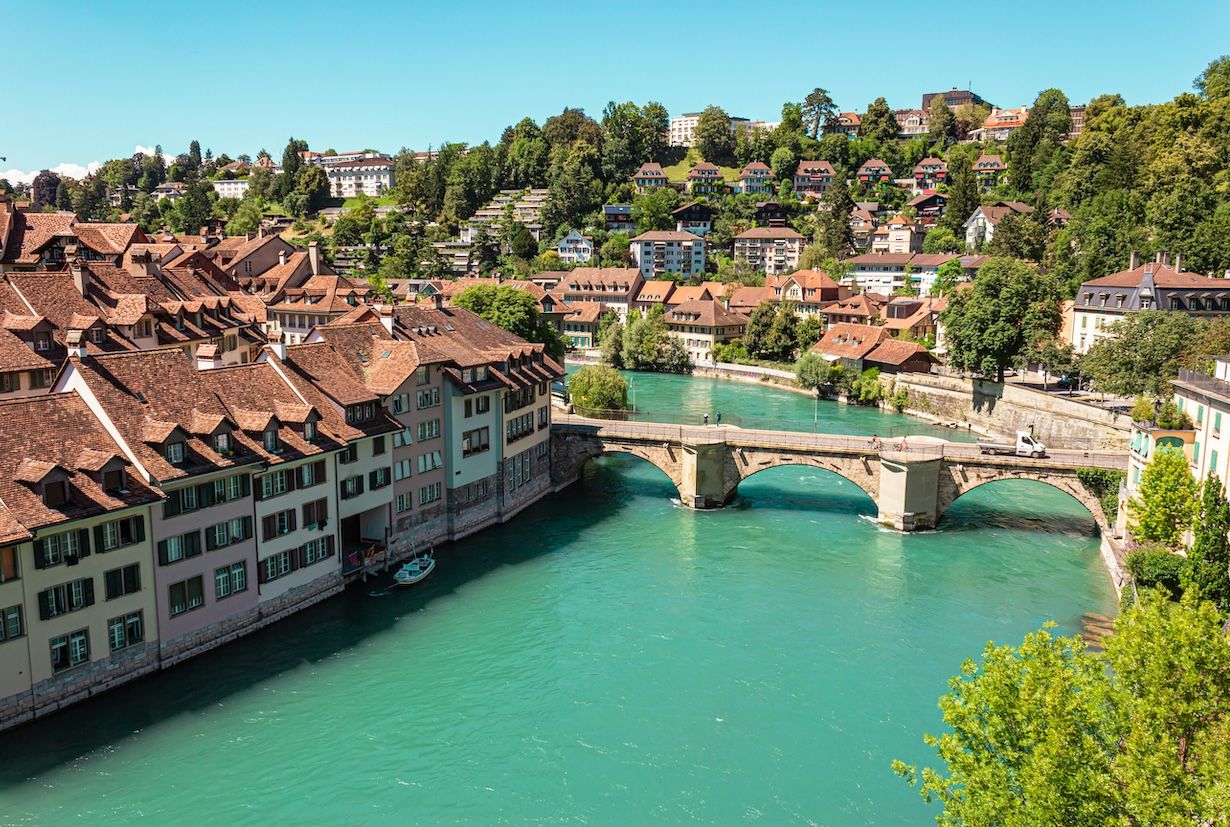 Blick auf die Altstadt von Bern mit der Aare und der historischen Brücke unter blauem Himmel.